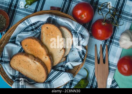 Cibo fresco naturale, ingredienti vegetariani italiani, pasta di spaghetti con aglio e pane tostato su un cesto su un panno da tavola, forchetta di legno di pepe verde Foto Stock