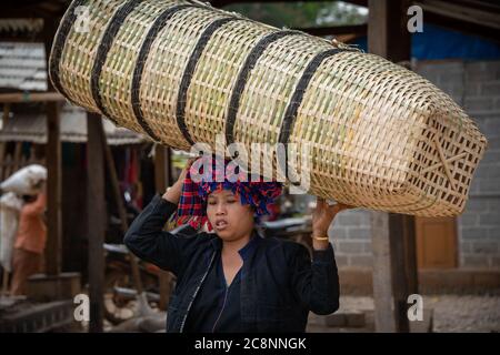 Maing Thauk, Myanmar - Febbraio 2020: Donna della tribù Pa-o porta un mucchio di cestini di vimini sulla sua testa nel mercato locale Foto Stock