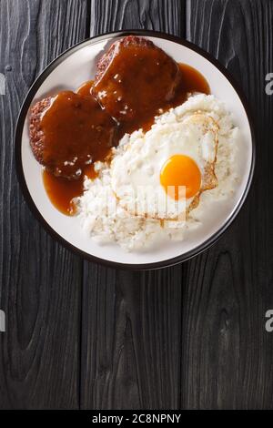 Il Loco Moco è un cibo hawaiano confortevole fatto con riso e un hamburger affumicato con salsa e uova da vicino su un piatto sul tavolo. Vista dall'alto verticale f Foto Stock