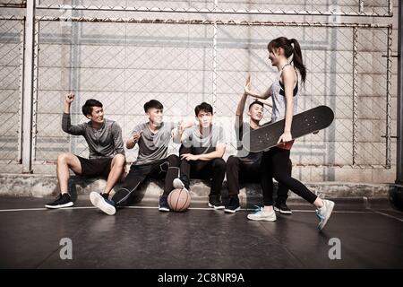 giovane donna asiatica adulta skateboarder dando un gruppo di giovani uomini hi-cinque Foto Stock