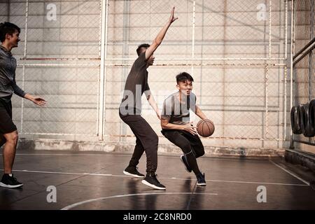 giovani uomini adulti asiatici che giocano a basket sul campo all'aperto Foto Stock