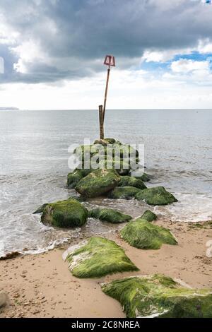 Onde che lambire sulle rocce di un groyne su Avon Beach Christchurch con l'Isola di Wight sullo sfondo Foto Stock