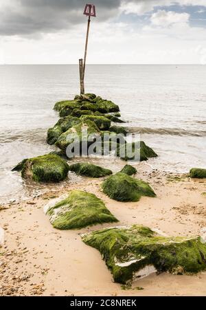 Onde che lambire sulle rocce di un groyne su Avon Beach Christchurch con l'Isola di Wight sullo sfondo Foto Stock