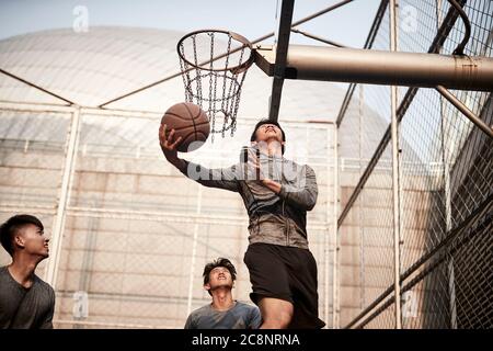 giovani uomini adulti asiatici che giocano a basket sul campo all'aperto Foto Stock