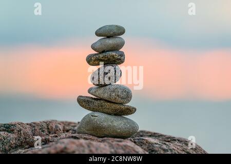 Un piccolo cairn posto su una roccia al tramonto con il sole che tramonta sullo sfondo Foto Stock