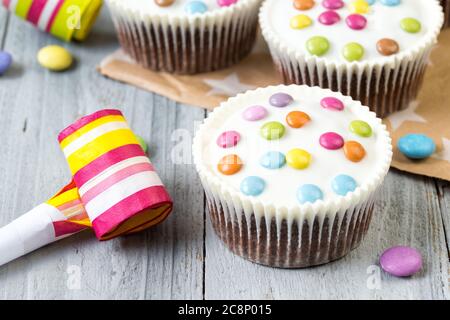 Cupcake al cioccolato con glassati e corno da festa, sfondo in legno Foto Stock