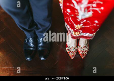 Vista che guarda giù sulle scarpe di sposa e sposo che indossa una miscela di abiti da sposa tradizionali cinesi e occidentali Foto Stock