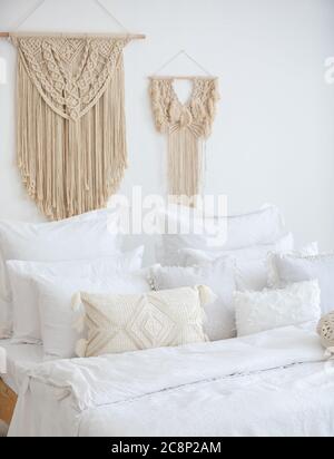 Immagine verticale di un letto sullo sfondo di una parete decorata con applique in macrame Foto Stock