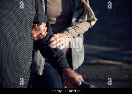 Coppia senior attiva all'aperto, donna che aiuta l'uomo a camminare lungo la strada. Foto Stock