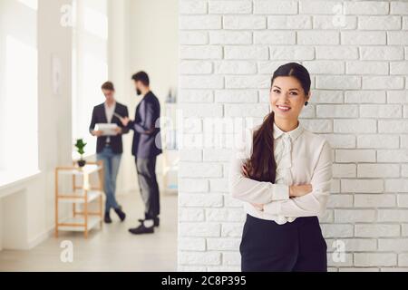 Donna d'affari latina ispanica sorridente mentre si trova in un ufficio bianco contro un muro bianco. Foto Stock