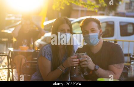 Spagna Madrid. Tostatura di coppia caucasica con birra che indossa una maschera sanitaria. Riaprire pub e club dopo quarentine coronavirus Covid-19. Uomo e donna dri Foto Stock