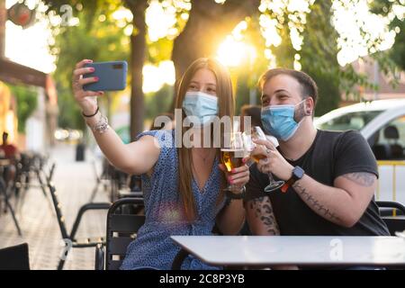 Spagna Madrid. Coppia caucasica tostatura con birra indossando maschera sanitaria prendendo un selfie. Riaprire pub e club dopo quarentine coronavirus Covid-19. M Foto Stock