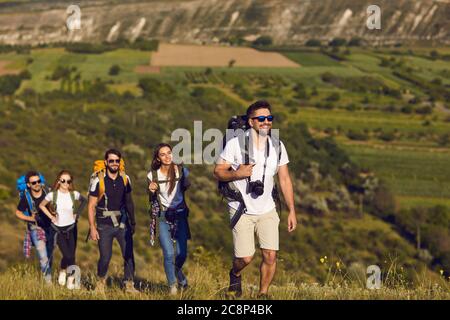 Un gruppo di amici con zaini in un'escursione nella natura. I turisti giovani camminano su una collina in montagna. Foto Stock