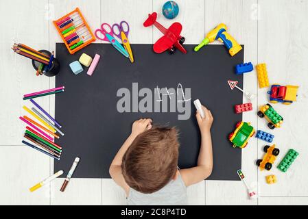 Il capretto disegna su un foglio nero di carta. Ragazzo che scrive una figura. Foto Stock