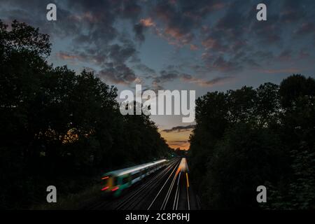 I treni si dirigono verso Brighton da Victoria sotto un tramonto incantevole Foto Stock