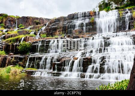 Bella, ampia cascata in un luogo turistico popolare. Un potente flusso d'acqua lungo le sponde rocciose, che si tuffa in un lago polveroso di verde. Lungo Foto Stock