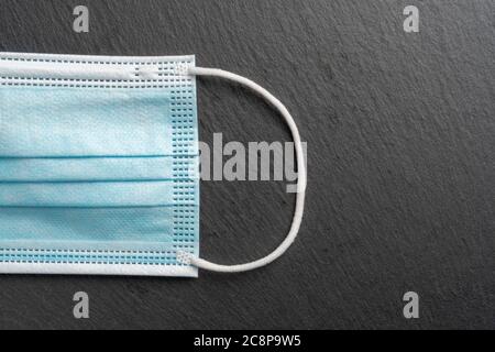 Parte di una maschera medica blu con fasce in gomma bianca sull'orecchio su uno sfondo grigio scuro. CopySpace. Per titoli e design Foto Stock
