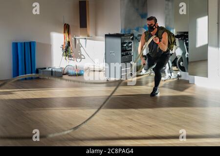 Sportivo in corda con maschera da allenamento. Interno su pavimento in quercia con sole e ombra. Per il concetto di boot camp. Foto Stock