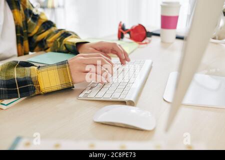 Immagine ravvicinata di un adolescente in camicia di plaid che lavora sul computer alla sua scrivania a casa Foto Stock