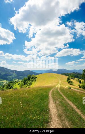 paesaggio rurale in un giorno d'estate. strada sterrata nei campi erbosi e colline ondulate. nuvole soffici su un cielo blu bellissimo scenario di falesia montagnosa Foto Stock