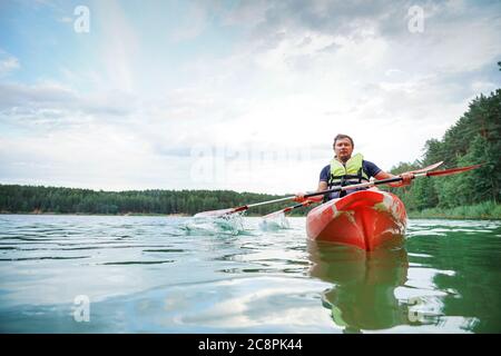 Guy in un kayak rosso galleggia lungo il fiume, in giubbotti di salvataggio Foto Stock