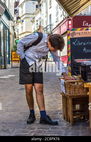 Giovane uomo che naviga libri di seconda mano fuori libreria su strada stretta della città, Loches, Indre-et-Loire, Francia. Foto Stock