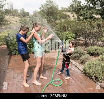 i bambini si spruzzano l'uno con l'altro con il tubo flessibile dell'acqua Foto Stock