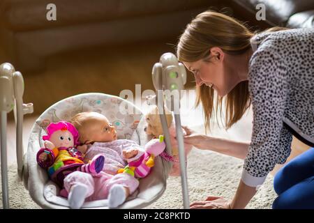 Donna che gioca con il bambino circondato da giocattoli che giacciono nell'oscillazione del bambino Foto Stock