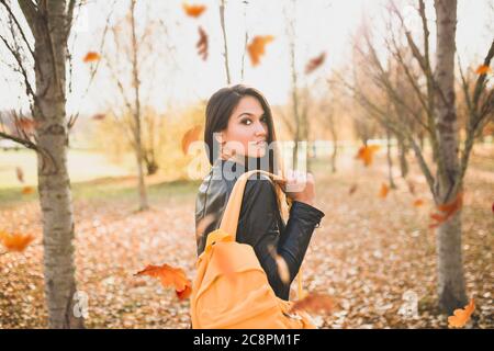 Bella bruna ragazza con zaino arancione si gira in un parco autunno - colori autunnali Foto Stock