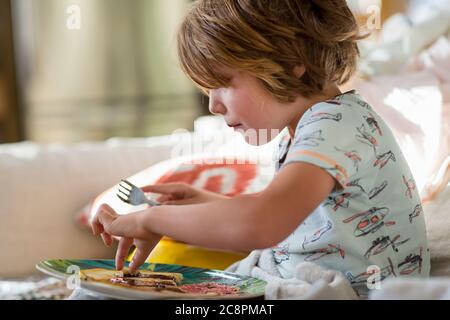 ragazzo di 4 anni che mangia frittelle sul divano Foto Stock