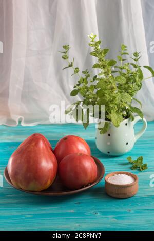 Pomodori rosa di campagna, grandi e maturi, su un tavolo di legno blu. Nella tazza - un mazzo di Melissa Foto Stock