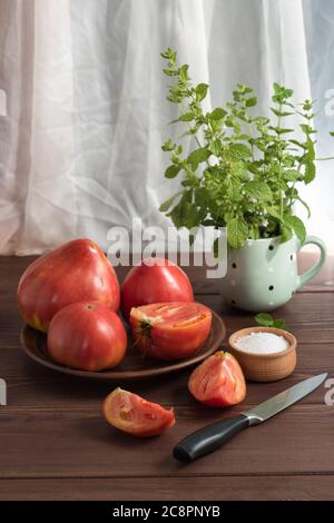 Grandi pomodori rosa di campagna dolci maturi e un salamoia su un tavolo di legno. Nella tazza - un mazzo di Melissa Foto Stock