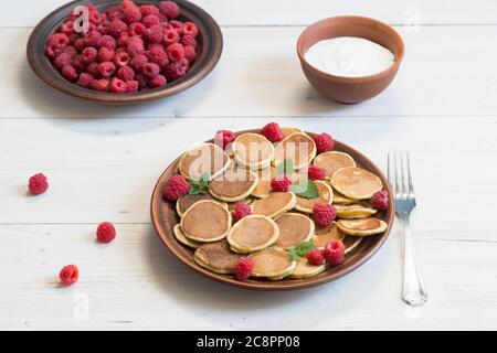 Pancake cereali con yogurt e lamponi freschi maturi in un piatto marrone su un tavolo di legno bianco. Deliziosa colazione estiva Foto Stock