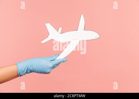 Profilo Vista laterale primo piano della mano umana in guanti chirurgici blu che tengono carta dell'aeroplano. Interno, studio shot, isolato su sfondo rosa. Foto Stock
