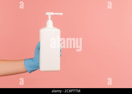 Profilo Vista laterale primo piano della mano umana in guanti chirurgici blu che tengono e mostrano disinfettante, antisettico o sapone antibatterico. Interni, studio shot Foto Stock