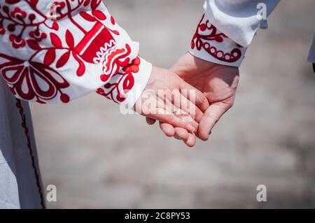 Gli sposi novelli tengono le mani vestite di ricamo rosso Foto Stock