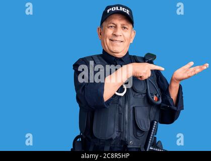 Uomo anziano bello che indossa uniforme della polizia stupito e sorridente alla macchina fotografica mentre si presenta con la mano e punta con il dito. Foto Stock