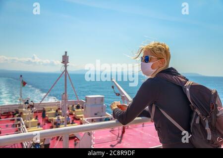 Donna in traghetto con maschera chirurgica durante il Covid-19 guardando panorama toscano. Viaggi turistici sul Mar Tirreno all'Isola d'Elba in traghetto Foto Stock