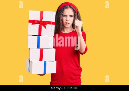 Carino ragazza ispanica bambino che tiene il regalo infastidito e frustrato gridando con la rabbia, urlando pazzo con la rabbia e la mano sollevata Foto Stock