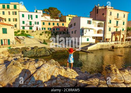 Felice turista donna godendo sopra le scogliere a Marciana Marina in Borgo al Cotone, isola d'Elba, Italia famose case di vecchio villaggio nella baia di Marciana Foto Stock