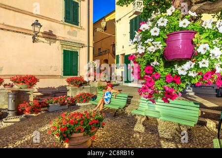 Donna seduta su panchina a Marciana Marina, fiorito vecchio quartiere Borgo al Cotone. Viaggi turistici in Italia. Marciana Marina, Isola d'Elba. Fiori di rosso Foto Stock