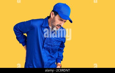 Bell'uomo di mezza età che indossa uniforme meccanica che soffre di mal di schiena, che tocca la schiena con la mano, dolore muscolare Foto Stock