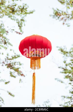 Lanterne rosse in tessuto fatte a mano isolate sulle foglie verdi e sullo sfondo del cielo bianco per il nuovo anno cinese in una chinatown Foto Stock