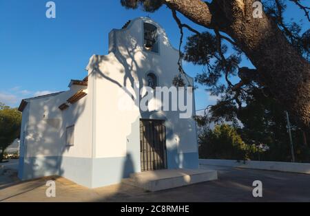 Cappella bianca 'Ermita de Sant Vicent' illuminata dal sole con ombre dal grande vecchio albero a la Nucia, Costa Blanca, Spagna Foto Stock