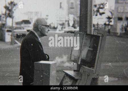 Fine anni '70 vintage nero e bianco stile di vita fotografia di un uomo anziano fuori per la sua passeggiata mattutina acquistare un giornale dalla locale edicola. Foto Stock
