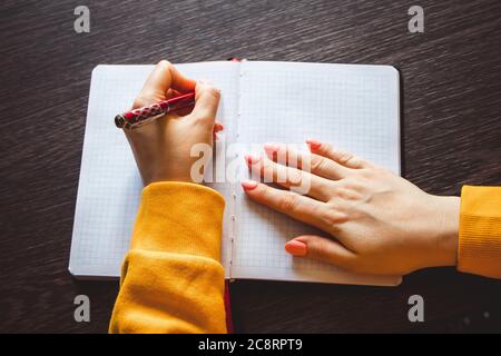 La giovane donna tiene una penna nella mano sinistra e scrive una nota in un taccuino vuoto. Giornata internazionale dei sinistri Foto Stock