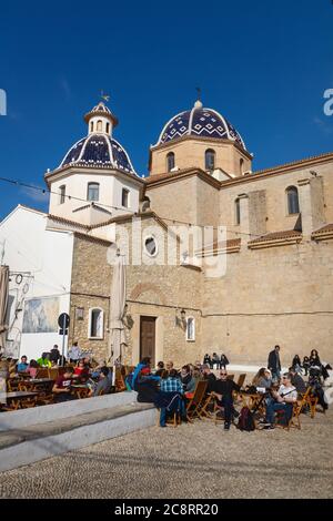 Altea, Costa Blanca, Spagna - 4 gennaio 2020: Visitatori stiting sulla terrazza ristorante di fronte alla chiesa a cupola blu della piazza della città vecchia Foto Stock