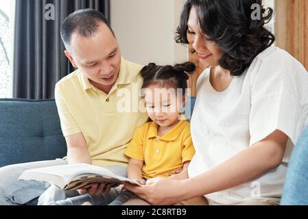 Sorridente madre vietnamita e padre mostrando interessante libro a Little Daughetr Foto Stock