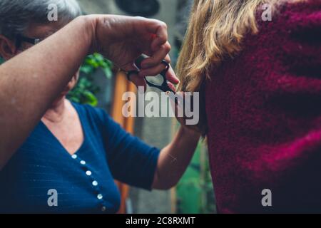 Una donna anziana sta tagliando i capelli di un giovane womans all'aperto Foto Stock