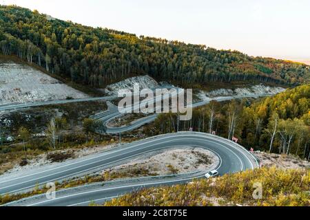 Strada pericolosa nei pressi della località di Belokurikha. Strada a serpentina in montagna di Altai in una giornata luminosa e soleggiata, sotto è un'erba verde e un asfalto Foto Stock